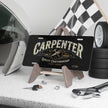 Black license plate with 'Carpenter' design on a stand, surrounded by automotive items.