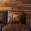 Decorative pillow with 'Carpenters That Build America' design on a leather sofa against a wood plank wall.