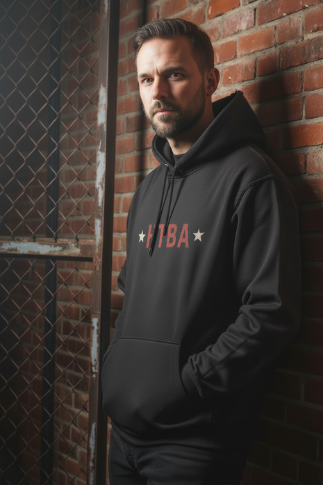 Man wearing a black hoodie with 'TBA' logo against a brick wall.