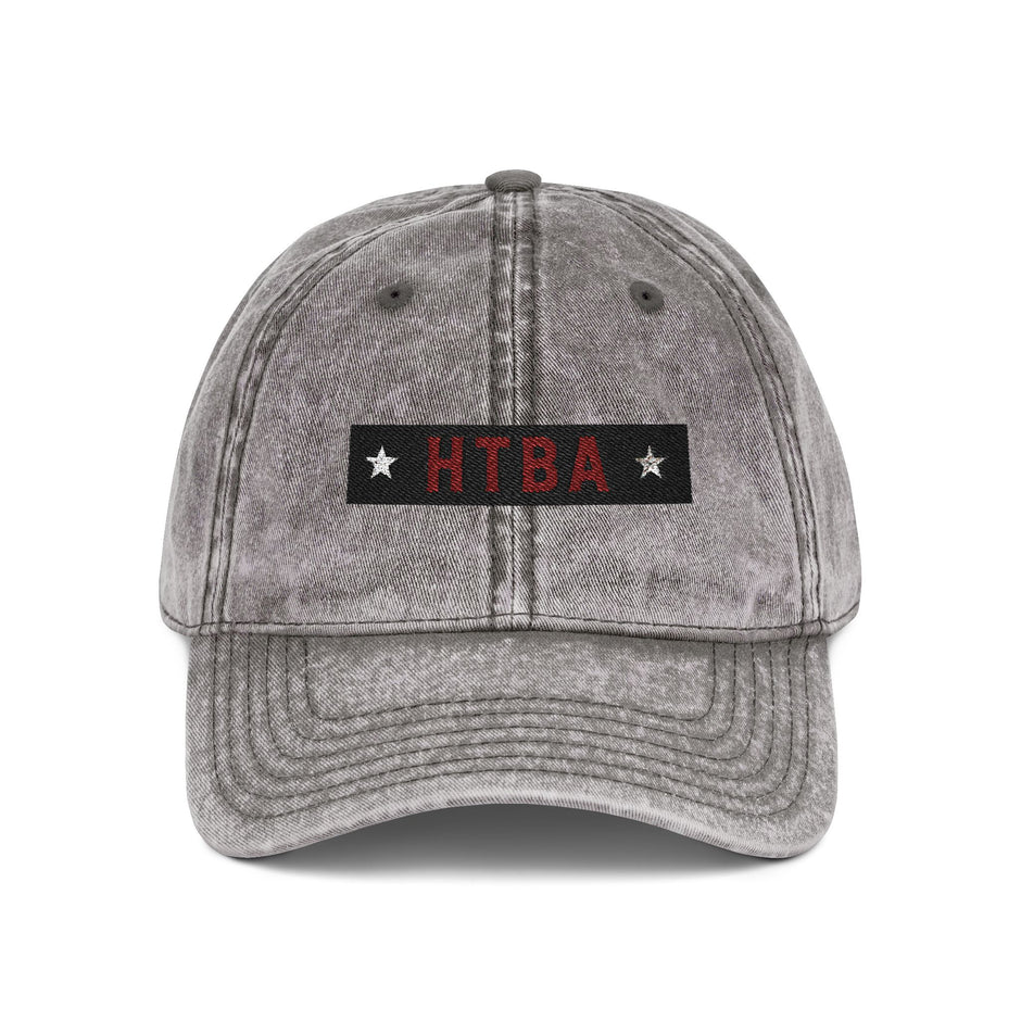 Gray denim cap with 'HTBA' logo on a white background