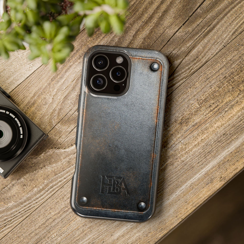 Phone case with 'HBA' logo on a wooden surface next to a camera and plant