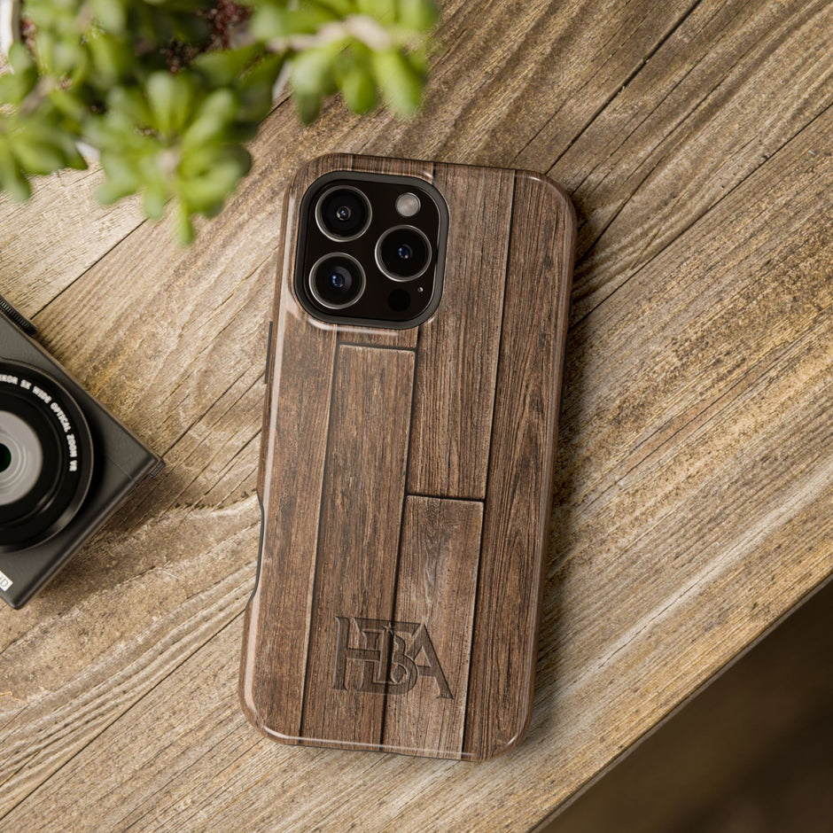 Wooden phone case with 'HTBA' branding on a wooden surface next to a camera and plant.