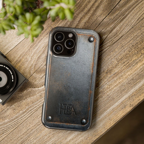 Phone case with 'HBA' logo on a wooden surface next to a camera and plant
