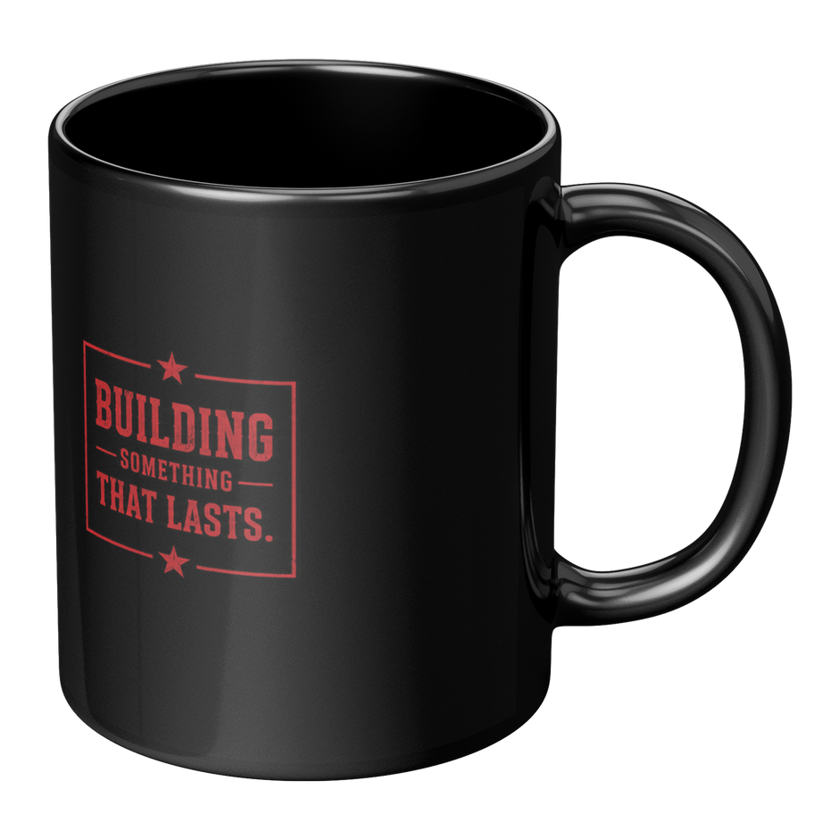 A glossy black ceramic mug with a red printed graphic on the front that reads 'BUILDING SOMETHING THAT LASTS.' with small star accents, shown on a plain white background.