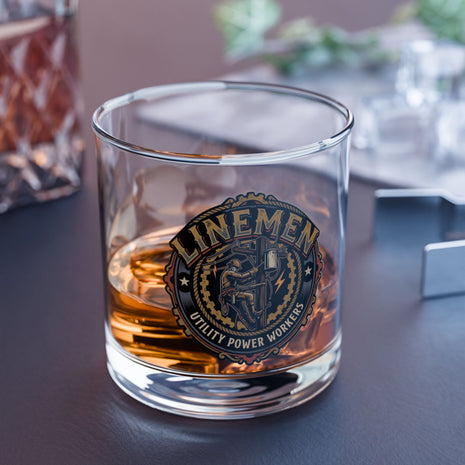 Glass with a 'Linemen' emblem filled with a amber liquid on a dark surface.