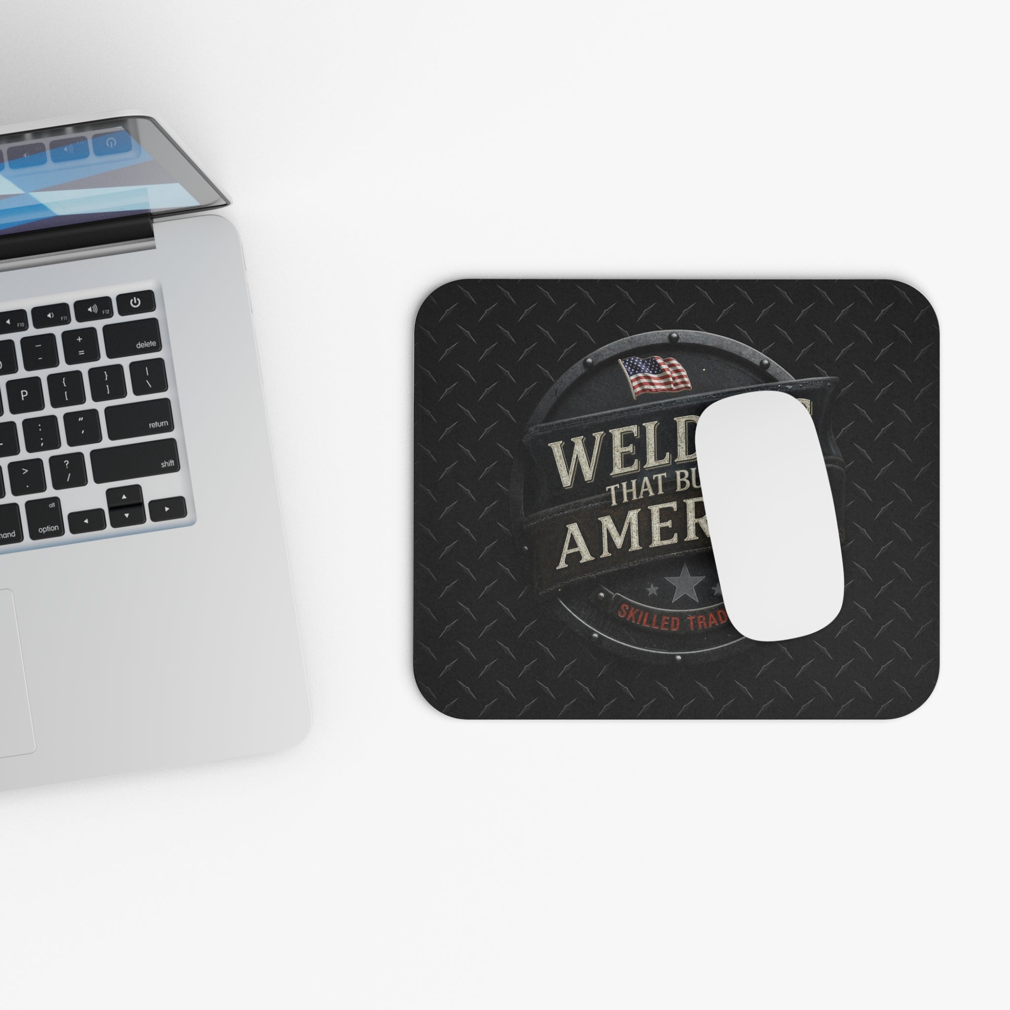 Mouse pad with Welders That Build America' design next to a laptop on a white surface