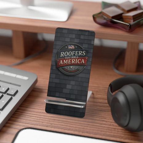 Phone stand with 'Roofers That Build America' logo on a desk with computer and headphones.