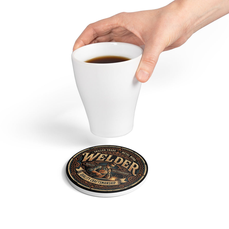 A hand holds a white ceramic coffee mug above a round coaster printed with the Welder brand logo and the phrase 'Quality Craftsmanship.' The mug is positioned above the coaster on a clean white background.