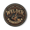 A circular graphic design featuring a vintage-style welder illustration with the word 'WELDER' in large letters, surrounded by decorative text and ornamental borders on a white background.