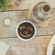 Welder coaster on a wooden table with a bottle and bottle cap.