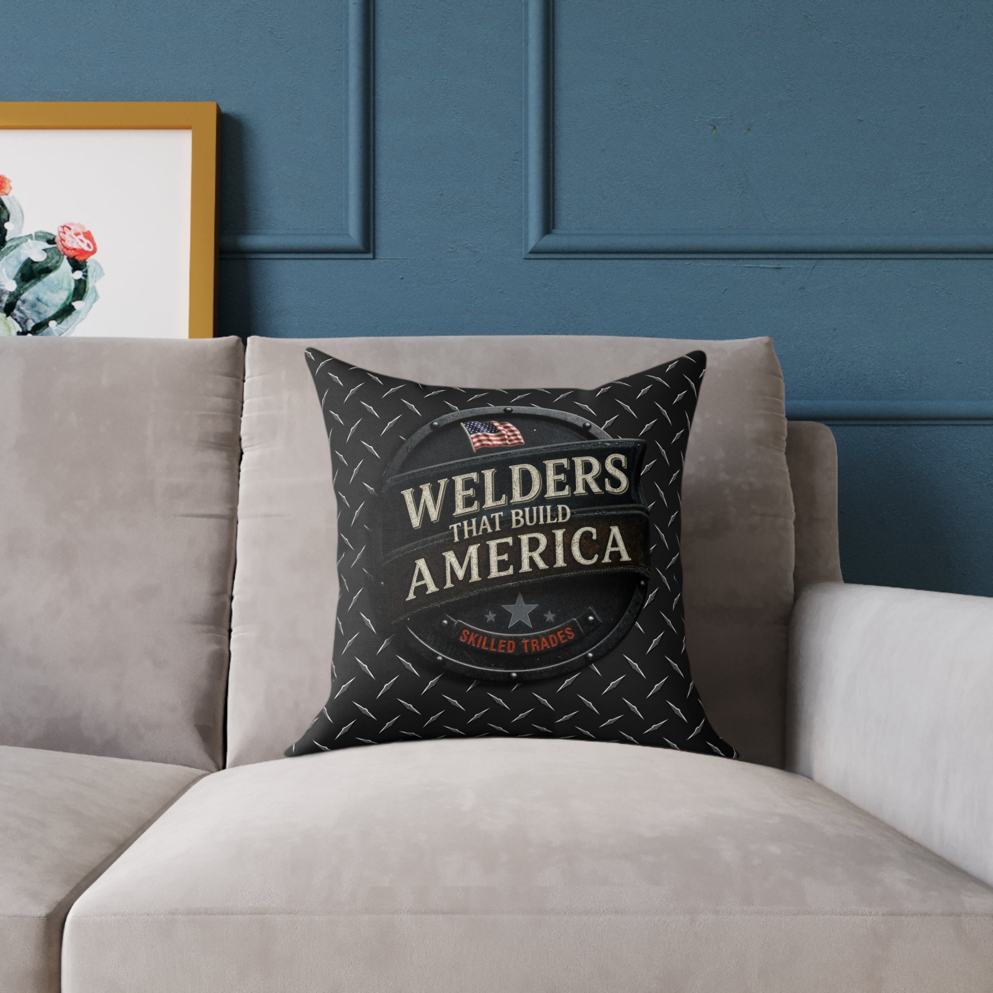 Decorative pillow with 'Welders That Build America' text on a gray couch against a blue paneled wall.